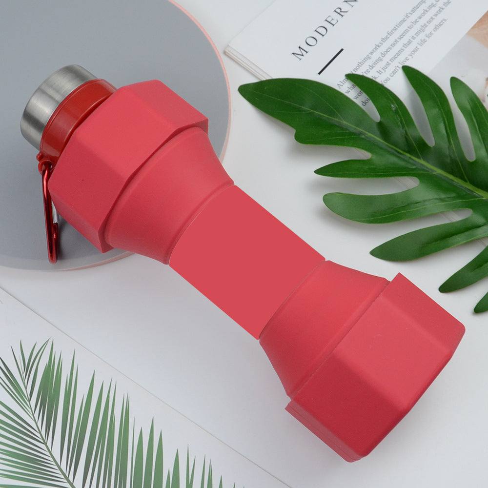 Red silicone sports bottle with collapsible dumbbell design on a decorative surface.