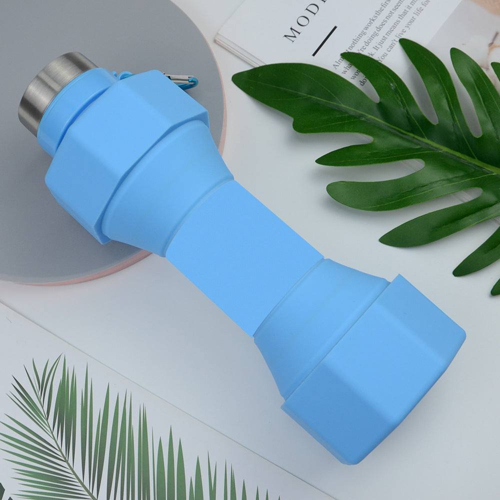 Blue silicone sports bottle with collapsible design on a table with leaves and a magazine.