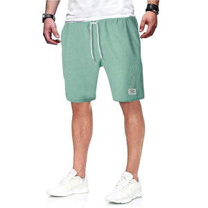 Man wearing green Simple Shorts with drawstring waistband and white sneakers.