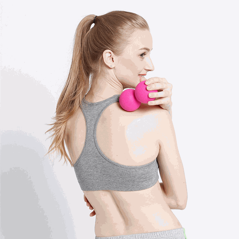 Woman using pink standard massage ball on her shoulder for muscle relief.